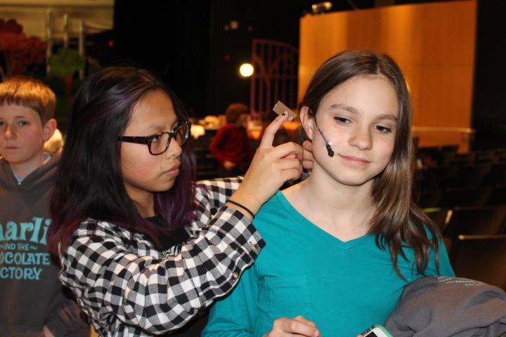 Eighth grade student director Glendy Cirolia carefully attaches a mic setup to 6th grade actor Natasha Taubenheim.  