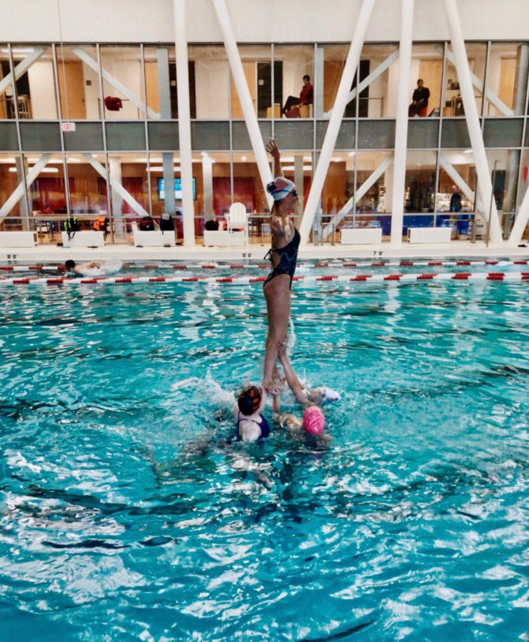 An eighth grader doing a lift, as the team members holding her up are treading water.